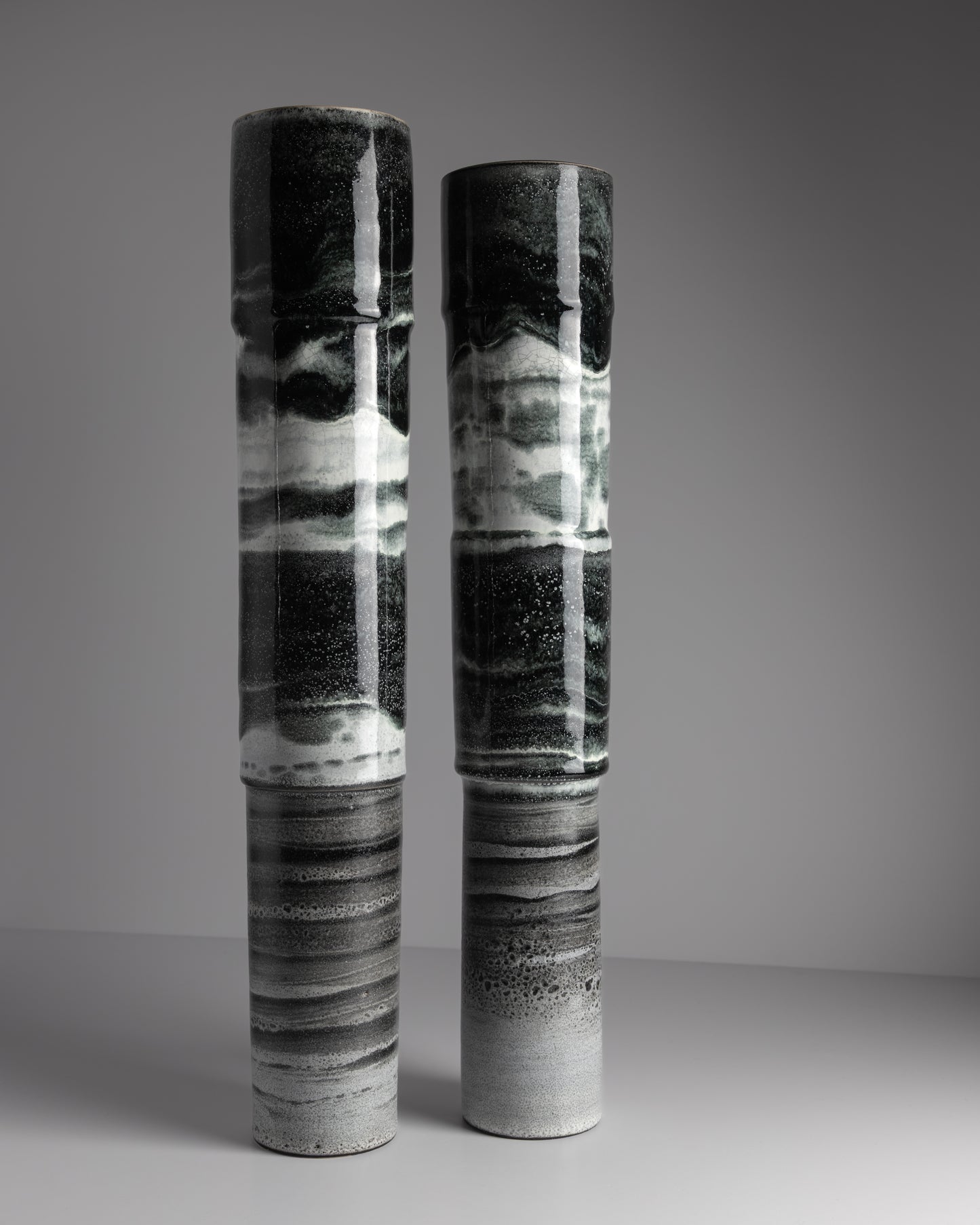 Two cylindrical ceramic vases with black and white abstract patterns on a gray background