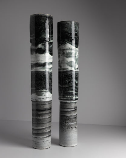 Two cylindrical ceramic vases with black and white abstract patterns on a gray background